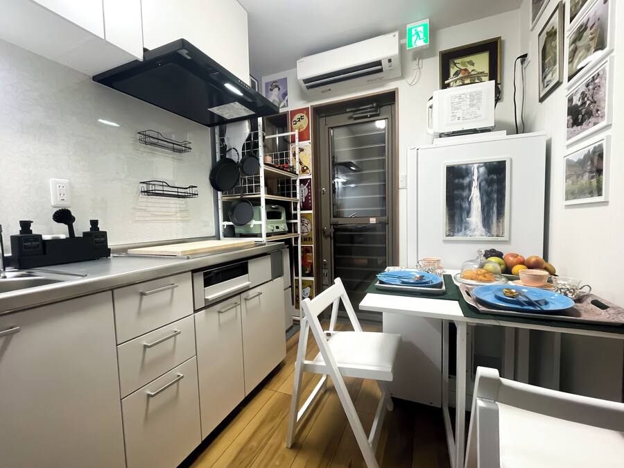 A modern kitchen with white cabinets, a black range hood, and a dining area with a white chair and table.