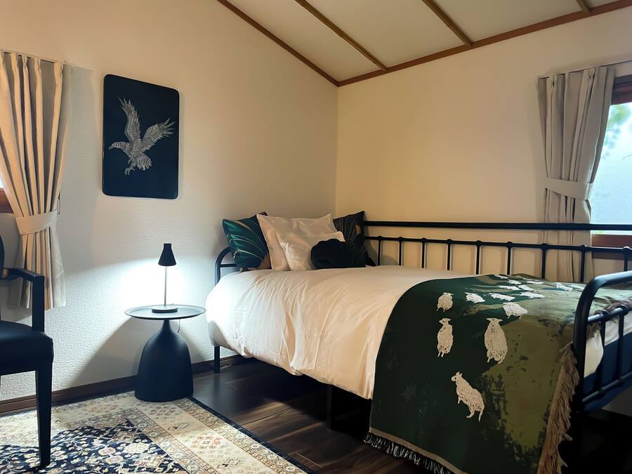 A neatly arranged bedroom with a bed, a small side table, a lamp, and a decorative wall piece.