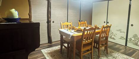 Un comedor con una mesa de madera dispuesta para cuatro personas, rodeada de sillas, un tapete estampado y una lámpara del techo.