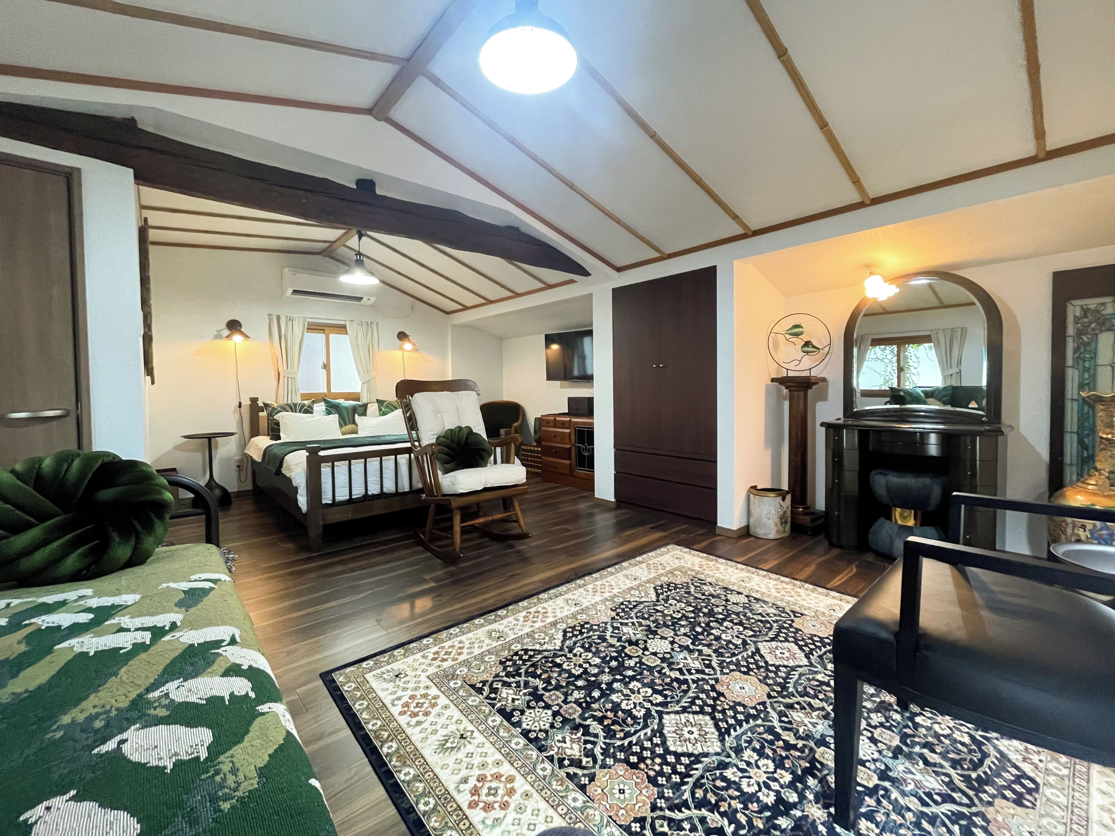A cozy room with a bed, a rocking chair, a large rug, and a mirror.