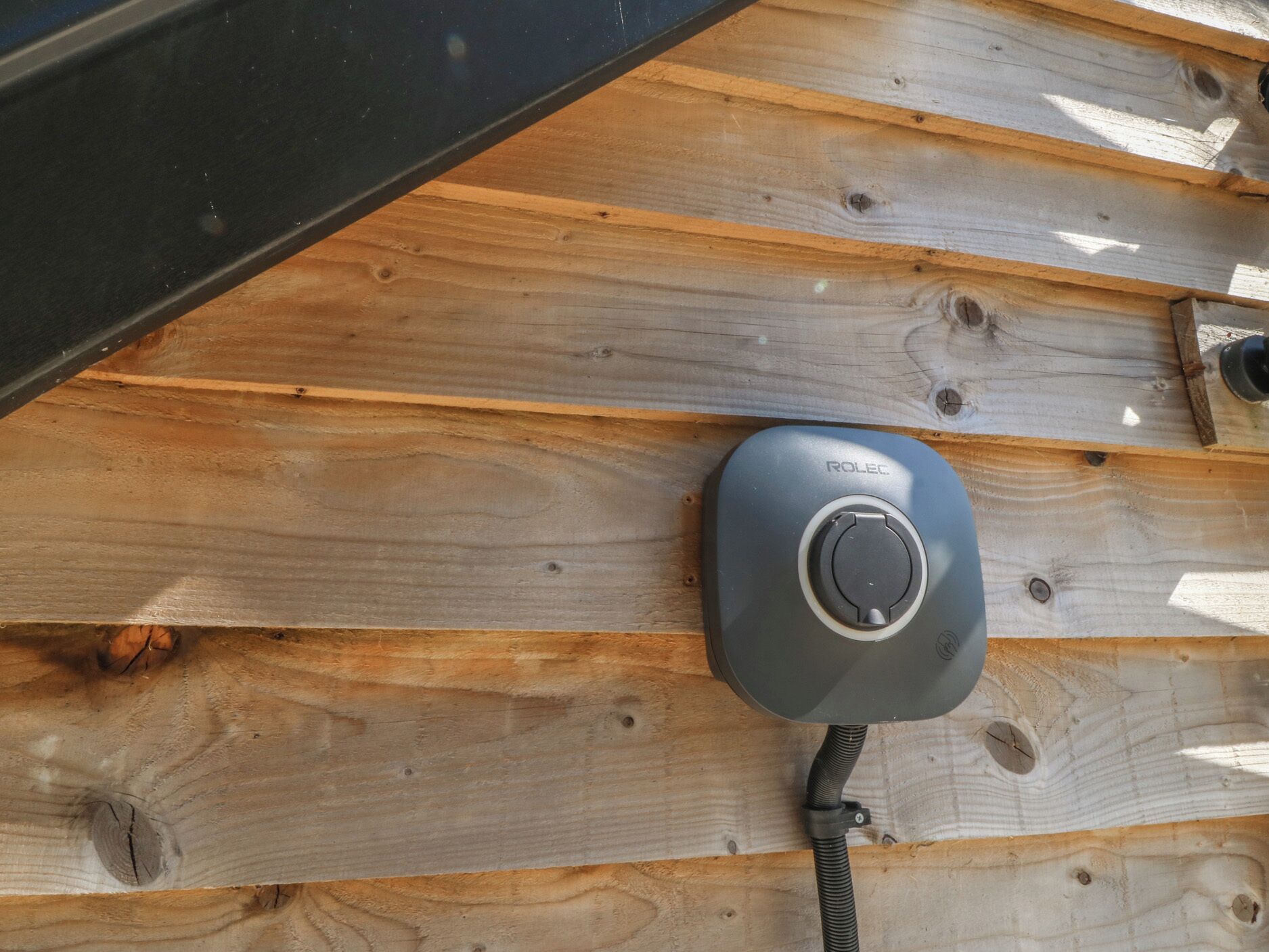 Un mur en bois avec un objet noir, qui pourrait être un appareil, et un câble.