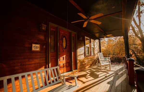 A wooden cabin with a porch, a ceiling fan, and a swing chair.