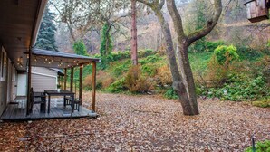 Un espace extérieur aménagé, abrité et doté de tables et de chaises, entouré d’un paysage naturel avec des arbres et une colline.