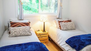 Une chambre avec deux lits, une table de chevet avec une lampe et une fenêtre avec des rideaux.