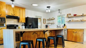 Une cuisine moderne avec des meubles en bois, un réfrigérateur noir, une cuisinière et des tabourets de bar.