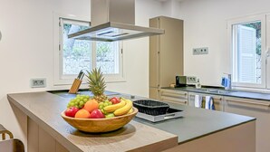 Une cuisine moderne dotée d’un îlot central, d’une hotte en acier inoxydable et d’une fenêtre laissant entrer la lumière naturelle.