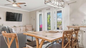 A modern living room with a wooden dining table, a sofa, and a TV mounted on the wall. - 30a Beach getaway, pool, Save 15% End of Summer (Santa Rosa Beach)