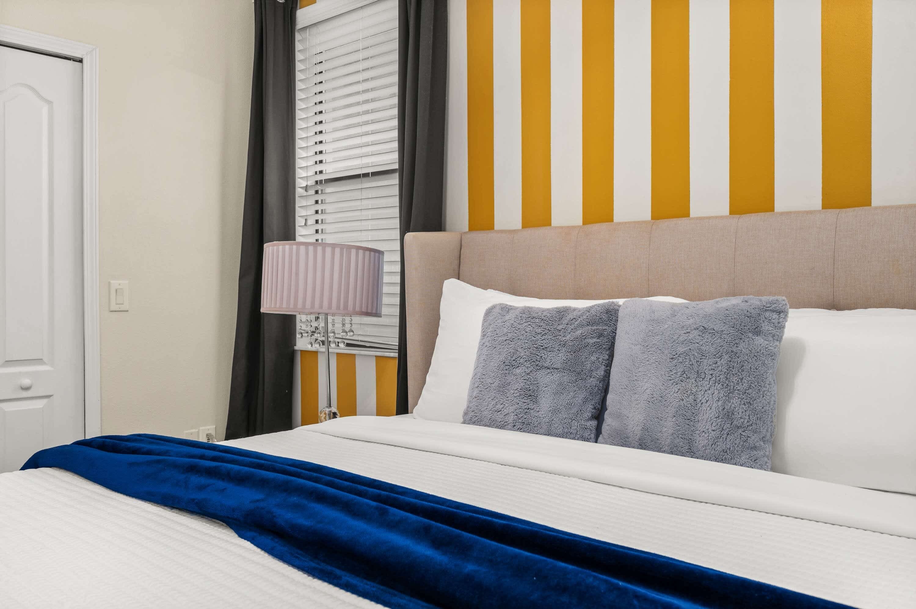 Une chambre d’hôtel avec un lit, une table de chevet, une lampe et une fenêtre avec des stores.