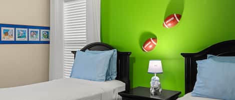 A hotel room with two beds, a nightstand with a lamp, and a green wall with sports-themed decorations.