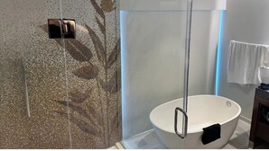 Ett modernt badrum med en duschavdelning med glasväggar, ett fristående badkar och en vägg täckt av mosaik.