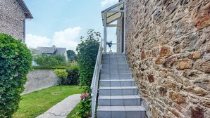 Una escalera de piedra que conduce a una puerta de cristal, rodeada de vegetación y un muro de piedra.