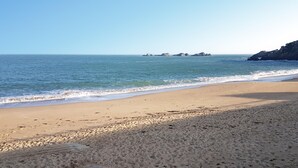 Una playa con cielos despejados, aguas tranquilas y afloramientos rocosos a lo lejos.