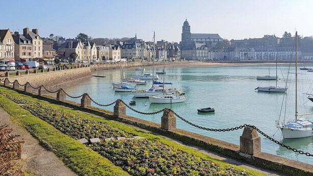 Un puerto con barcos, un paseo marítimo lleno de flores y edificios históricos al fondo.