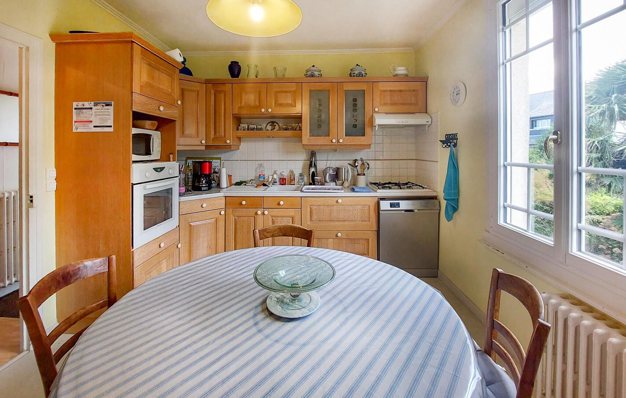 Una cocina con armarios de madera, estufa, microondas y una mesa de comedor con sillas.