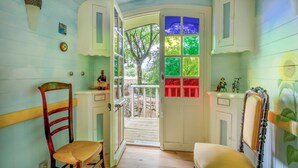 A room with a wooden floor, a chair, a table, a door with colorful glass panes, and a small balcony with a railing.