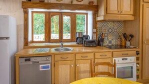 A kitchen with wooden cabinets, a built-in dishwasher, a coffee maker, a toaster, and a window with a view of greenery.