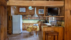 Eine rustikale Küche mit Holzschränken, einem weißen Kühlschrank, einem Esstisch mit Stühlen und einem kleinen Holztisch.