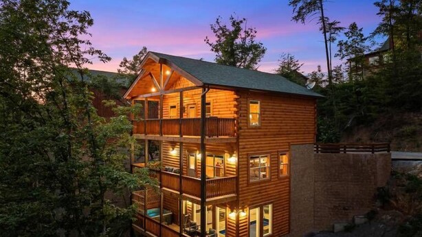 Una cabaña de troncos de varios pisos, con balcones y una terraza, rodeada de árboles.