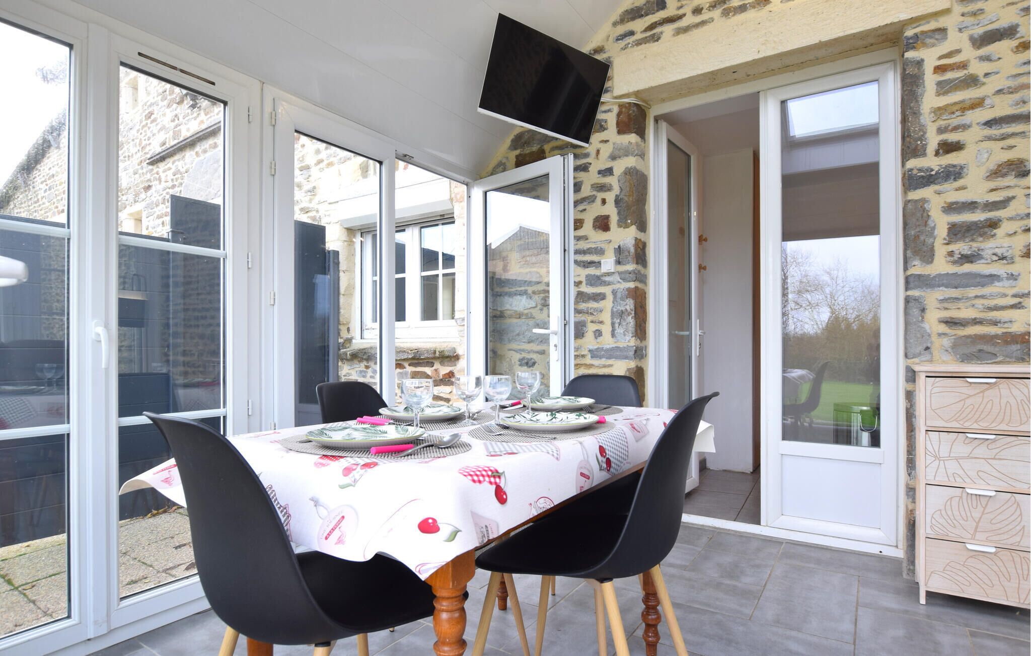 Un espace repas avec une table dressée pour quatre personnes, entouré de grandes fenêtres et de murs en pierre.
