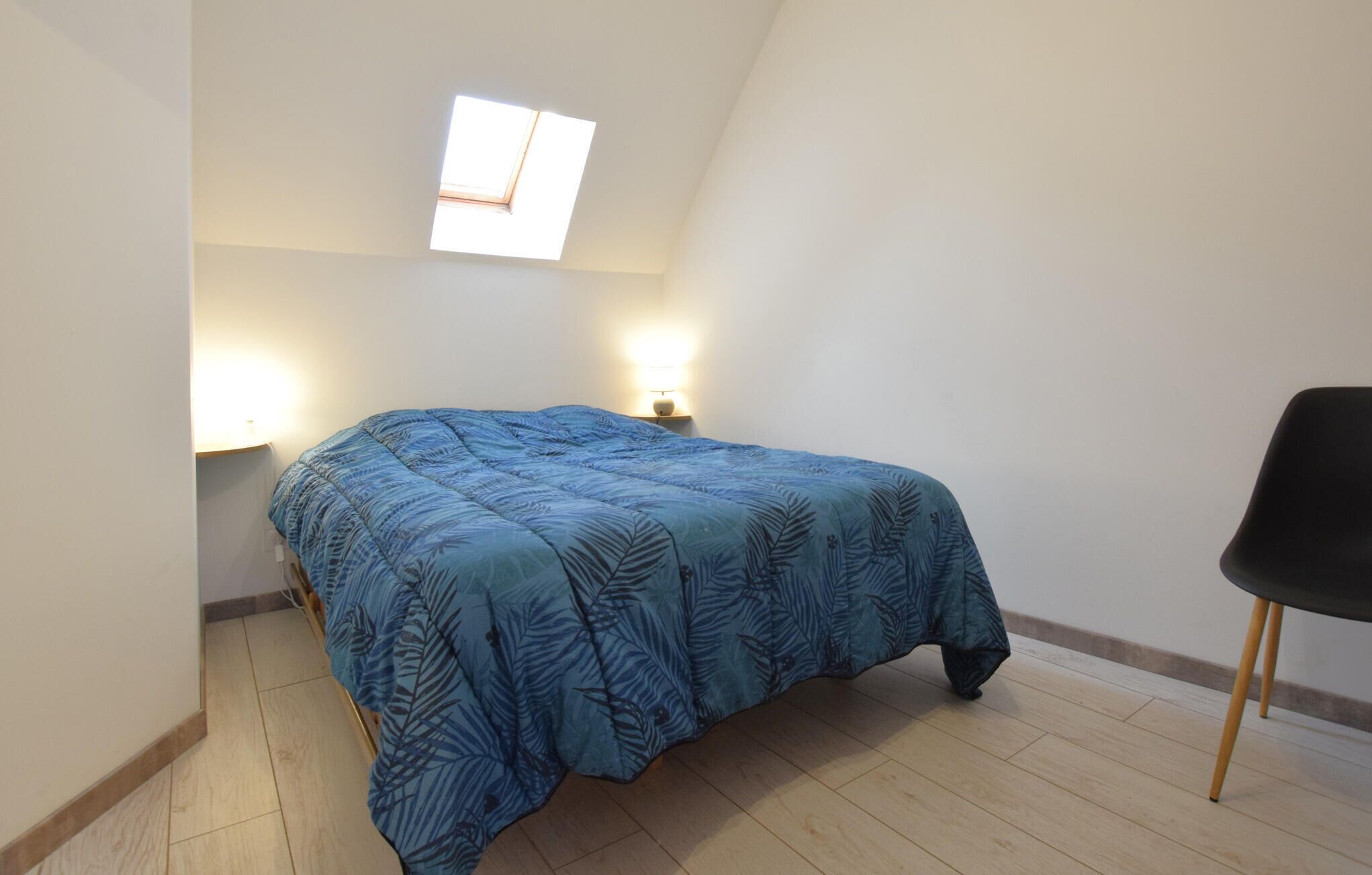 A small, simple room with a bed, a chair, and a skylight.