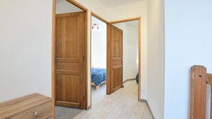 Een hal met houten deuren die leiden naar een slaapkamer met een bed en nachtkastje.