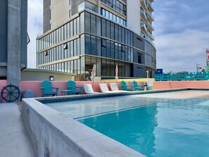 A swimming pool with lounge chairs and a ship's wheel, adjacent to a modern building with large windows and balconies. - The Wesley Playas de Tijuana Storybook by the sea (Tijuana)