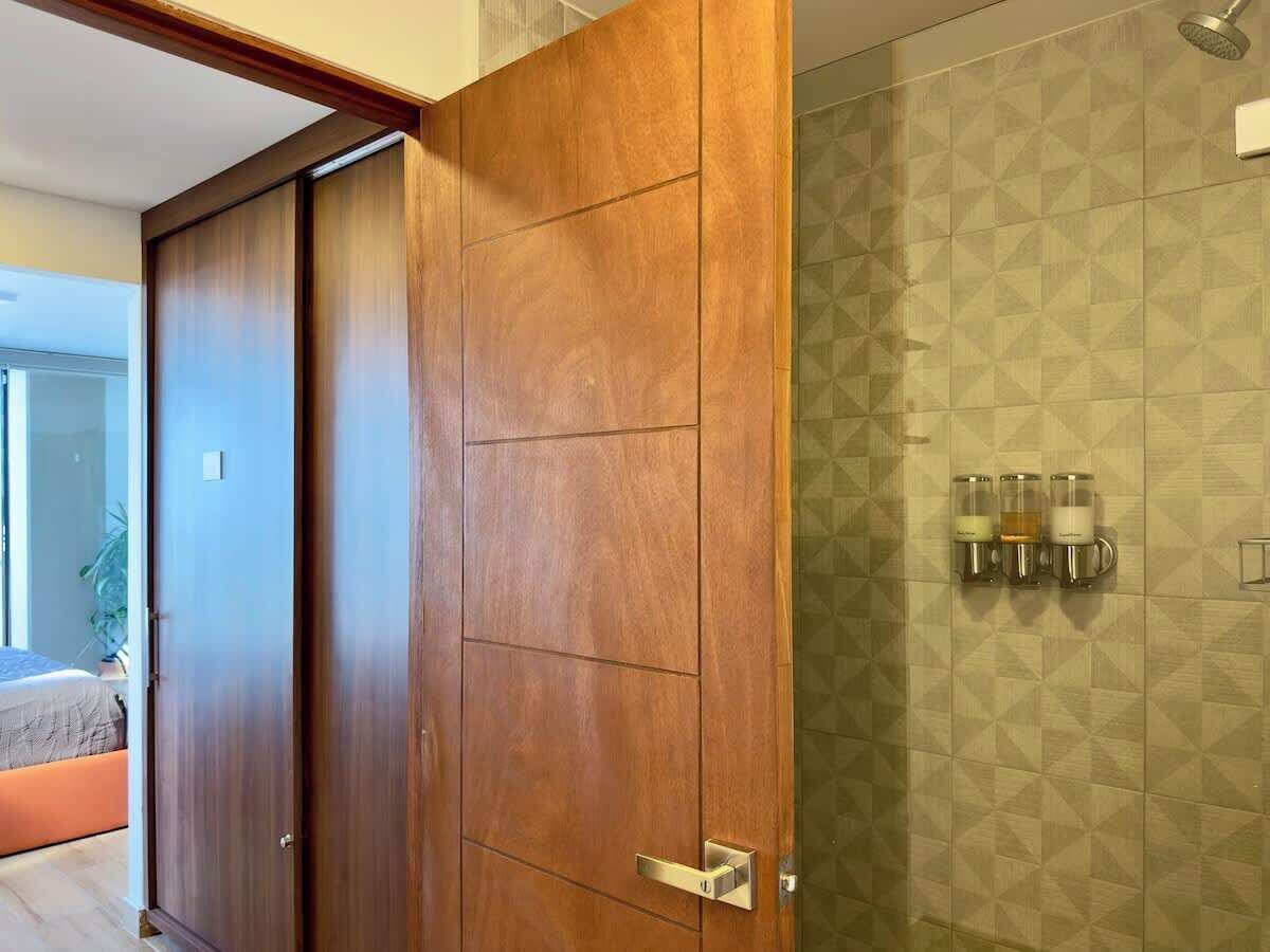 Eine Holztür führt zu einem Badezimmer mit Dusche und einer an der Wand befestigten Kaffeestation.