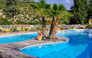 Ein Swimmingpool mit Liegestühlen und Palmen, umgeben von einem weißen Zaun und Blick auf eine Hügelkuppe.