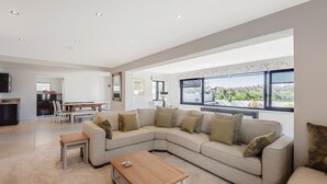 A spacious living room with a large L-shaped sectional sofa, a wooden coffee table, and a dining area with a table and chairs.