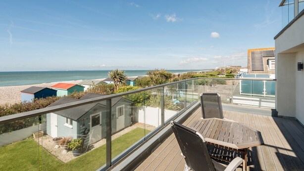 A balcony with a view of the sea, a wooden table, and a chair.
