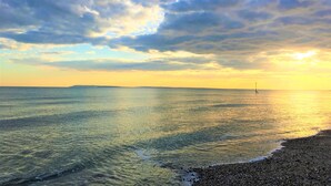 A beach with a pebbly shore and a clear sky with scattered clouds.