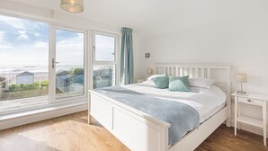A bedroom with a large window, a bed with pillows, a bedside table, and a hanging light fixture. - Beira Mar Beachfront Family Home | Pet-Friendly, Sleeps 8, Parking Included (East Wittering)