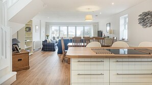 A spacious kitchen with a central island, wooden cabinets, and a view to the dining area. - Beira Mar Beachfront Family Home | Pet-Friendly, Sleeps 8, Parking Included (East Wittering)