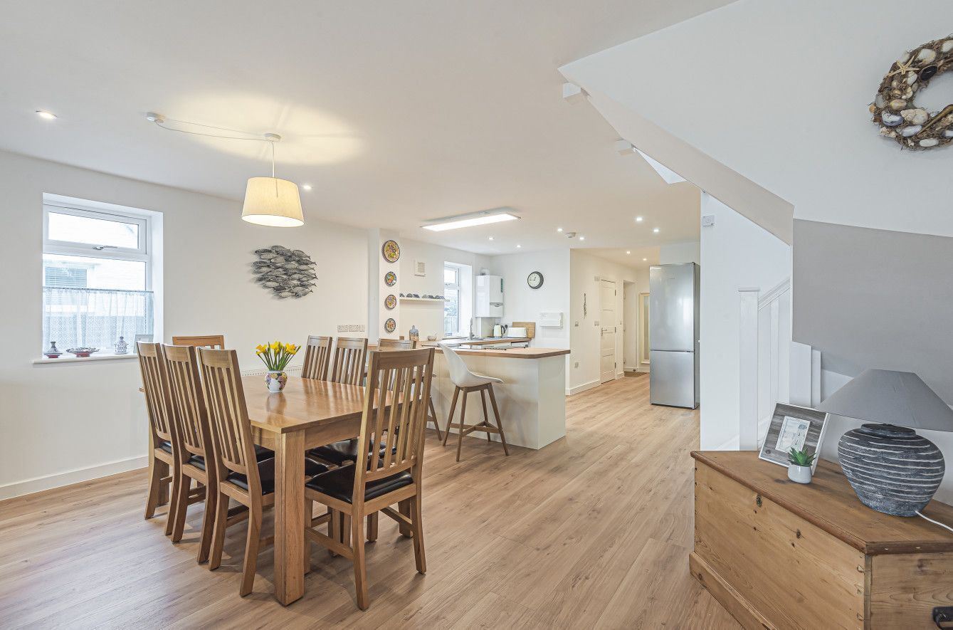 A spacious kitchen with wooden flooring, a dining area with a wooden table and chairs, and a modern pendant light.