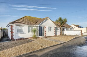 A two-story house with a tiled roof, a small front garden, and a gravel driveway. - Sunny Days: Bracklesham Bay Beach Bungalow – Sleeps 7, Parking & Dog Friendly (Bracklesham Bay)