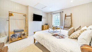 A bedroom with a bed, a wooden shelf, a television, a window, and a wooden ladder. - West Wittering Rosemary Cottage – Sleeps 5, Nr Beach, Parking & Family Friendly (West Wittering)
