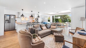 Ein modernes Wohnzimmer mit Ecksofa, Poufs und einem Essbereich mit Holztisch und Stühlen.