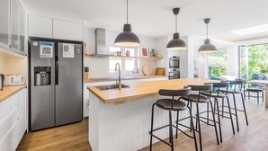 Eine moderne Küche mit einer zentralen Kochinsel, Edelstahlgeräten, Pendelleuchten und Blick ins Freie.