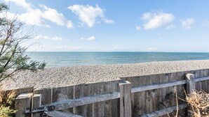 Una passerella di legno conduce a una spiaggia di ciottoli con vista libera sul mare.
