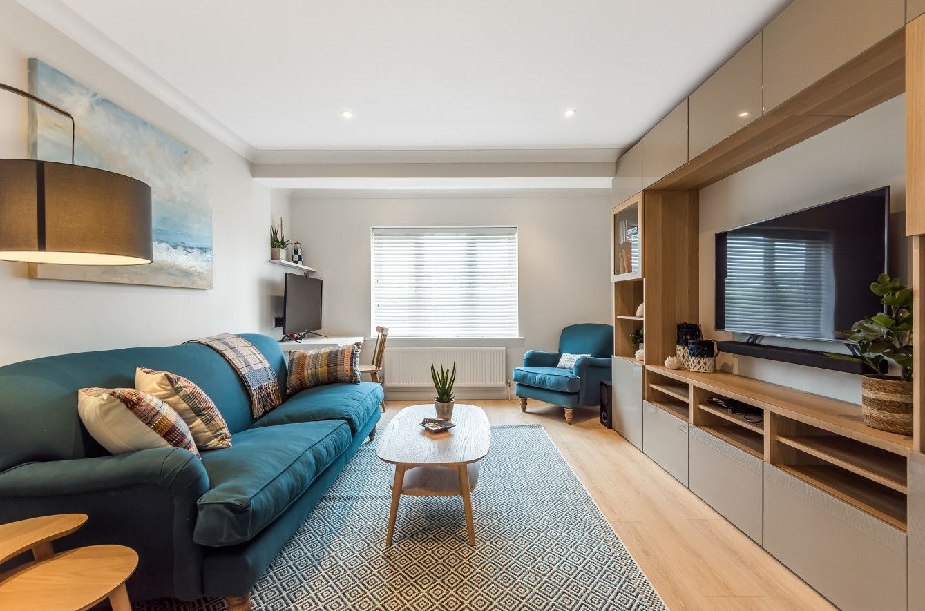 Un salon moderne avec un canapé bleu, une table basse, un téléviseur et une grande fenêtre équipée de stores.