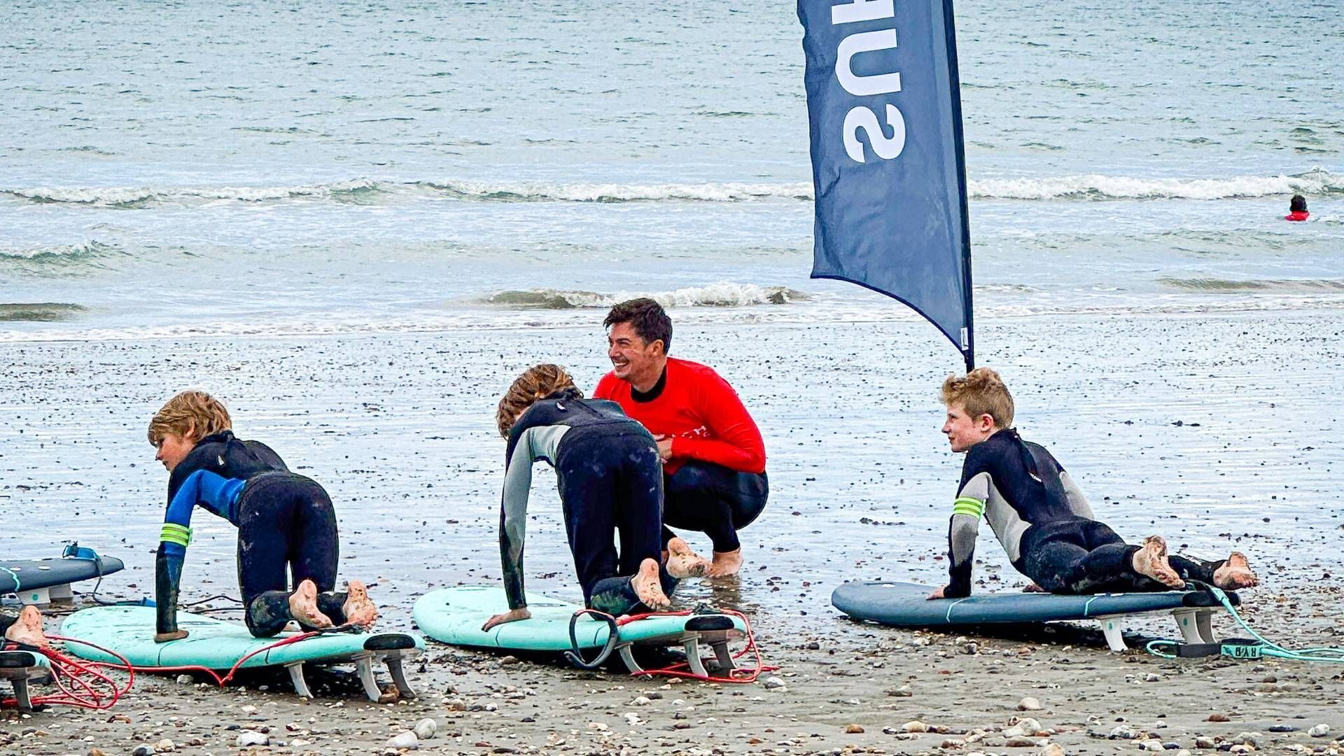 People on surfboards at a beach with a flag in the background.