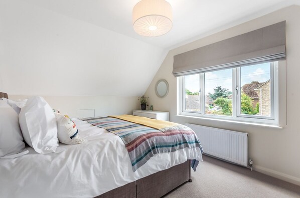 A bedroom with a bed, a window, a radiator, and a bedside table. - Little Orchard: West Wittering Home – Sleeps 10, 5 Bedrooms & Hot Tub (West Wittering)