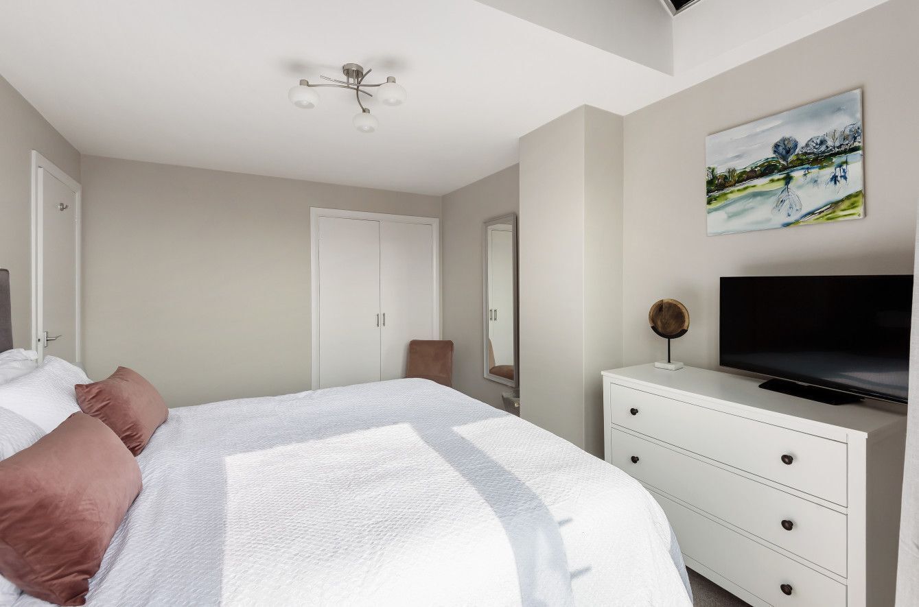 A bedroom with a bed, a dresser, a TV, and a painting on the wall.