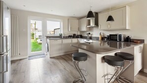 Een moderne keuken met een groot schiereiland, barkrukken, roestvrijstalen apparatuur en uitzicht op buiten.