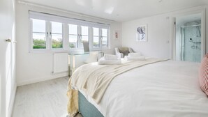 Un dormitorio con un ventanal grande, una mesa de vidrio, una cama con ropa de cama blanca y una zona de ducha.
