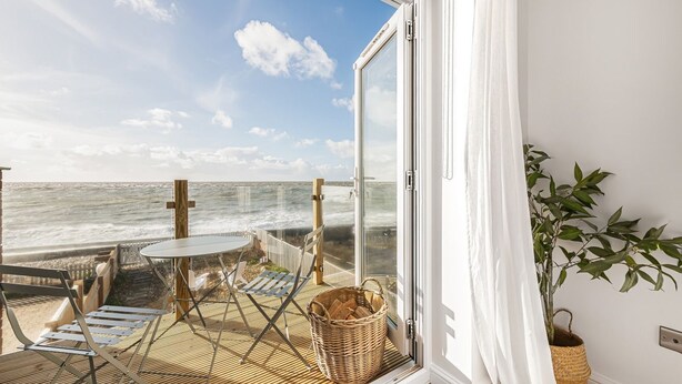 Un balcón con vistas al mar, una mesa, sillas y una cesta de mimbre.