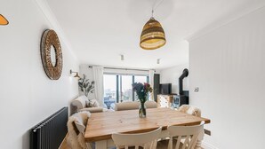 Un comedor con mesa de madera y sillas blancas, una lámpara colgante de mimbre y un radiador en la pared.