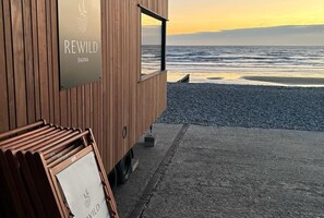 A wooden building with a sign reading 'REWILD SAUNA' and a view of the ocean. - The Waterfront: Luxury Bracklesham Bay Beachfront Home – Sleeps 8 (Bracklesham Bay)