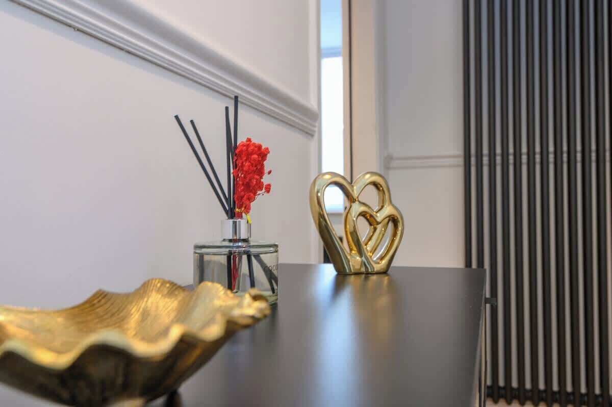 A table with a decorative gold tray, a glass container with red flowers and black sticks, and a golden heart-shaped object.