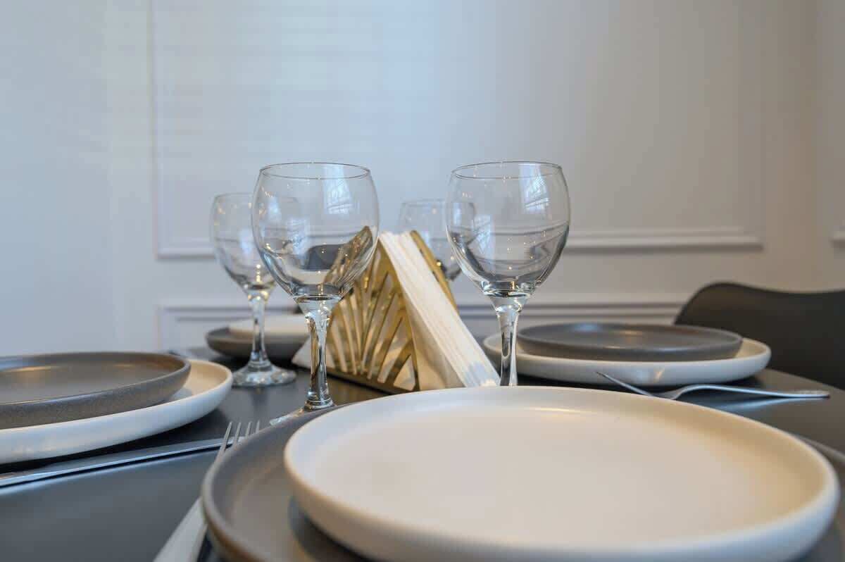 Mesa de jantar posta com pratos, talheres e copos de vinho, com um vaso decorativo ao centro.